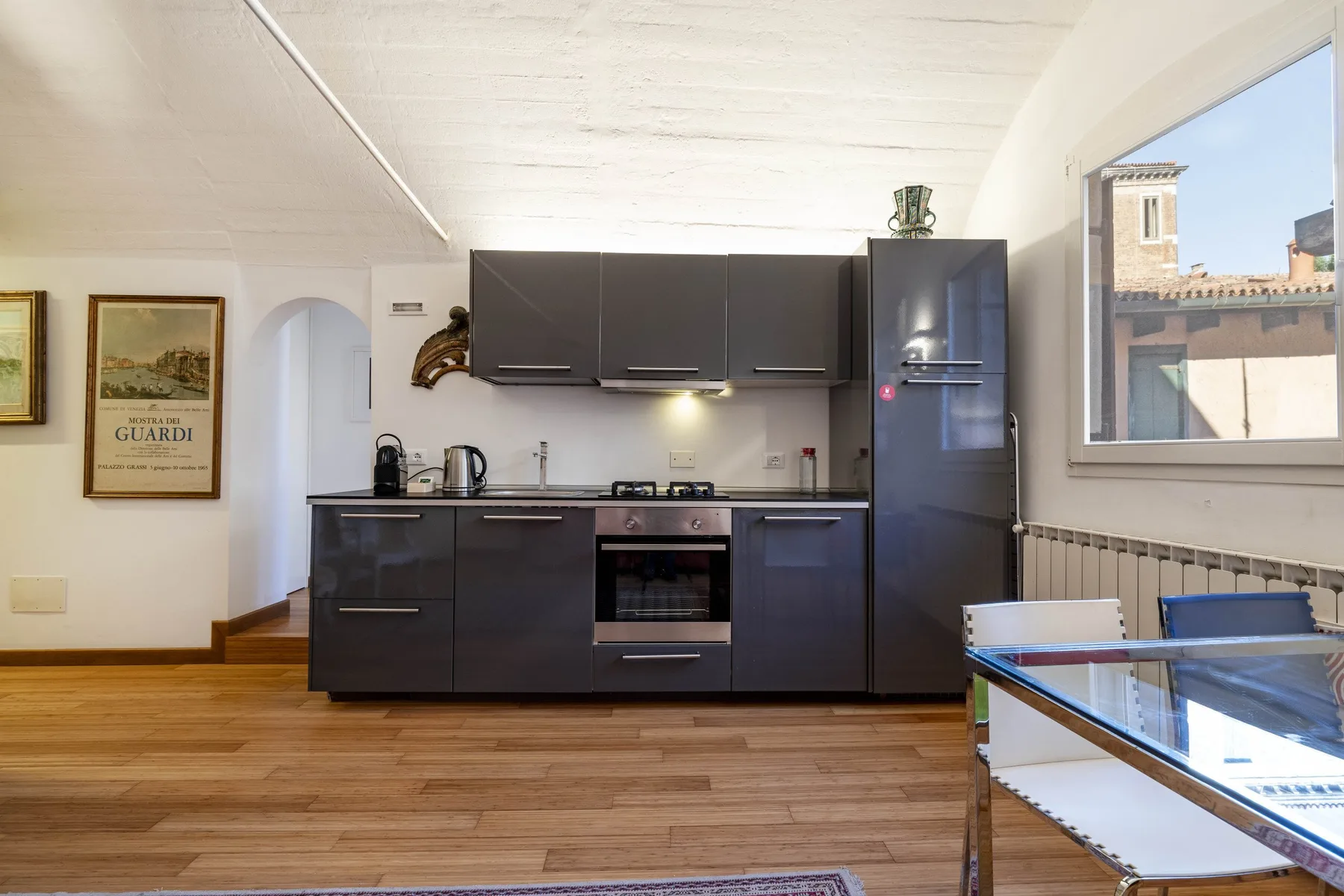 A modern kitchen with dark cabinets, a built-in oven, and a large window.
