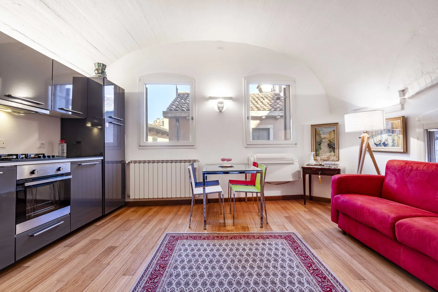 A bright living room with a kitchenette, dining table, and red seating.