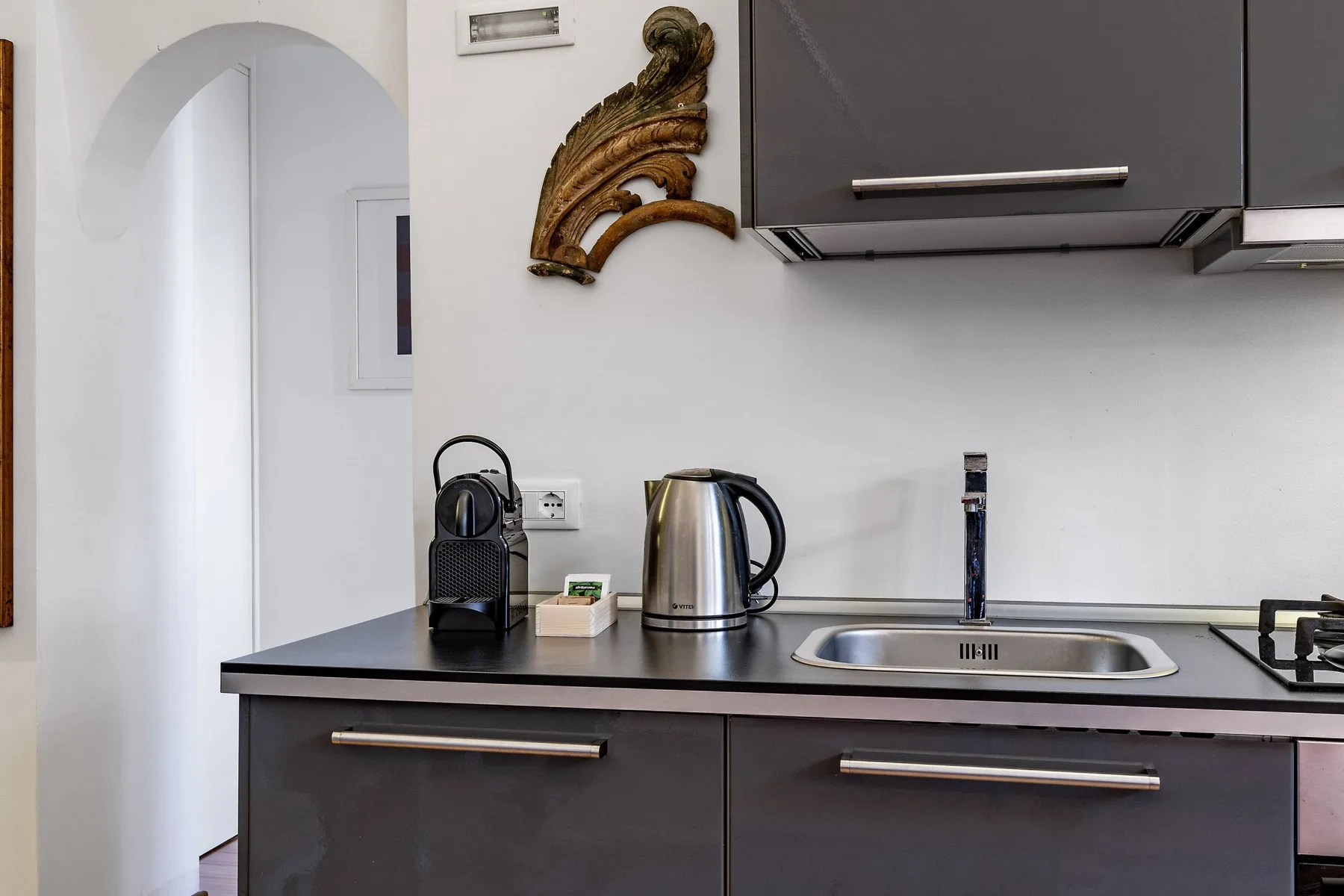 A kitchen counter with a kettle, coffee maker, and sink.