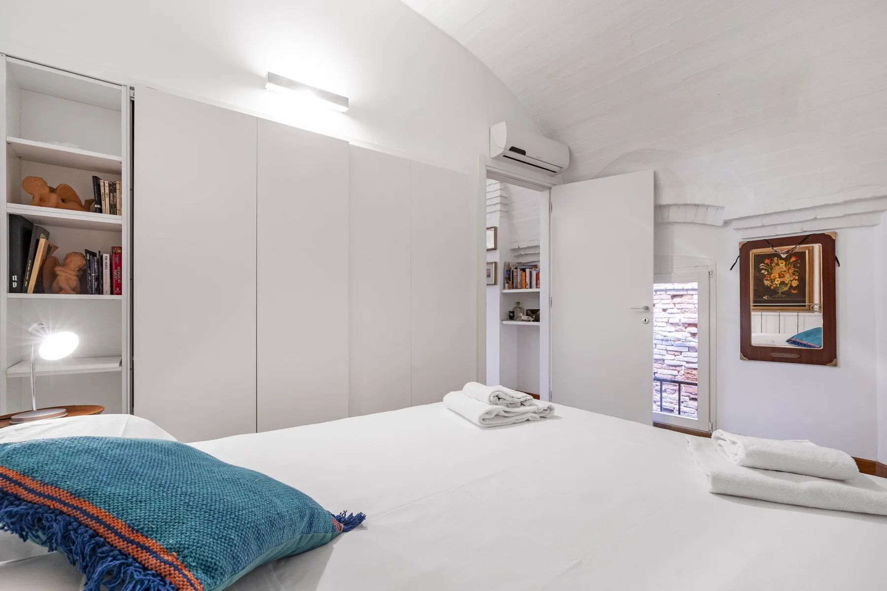 A bedroom with a neatly made bed, built-in storage, and an open doorway.