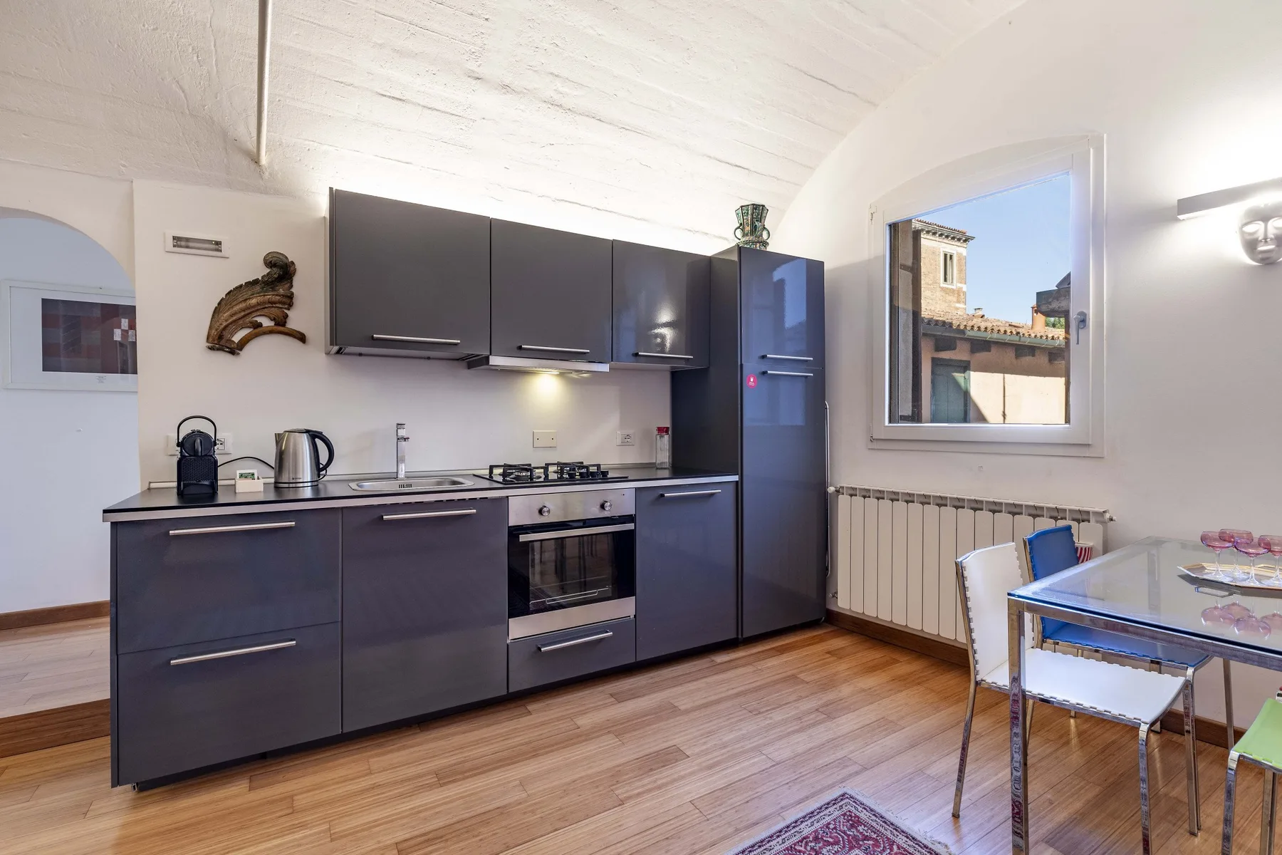 A modern kitchen with dark cabinets, cooking appliances, and a dining table by the window.