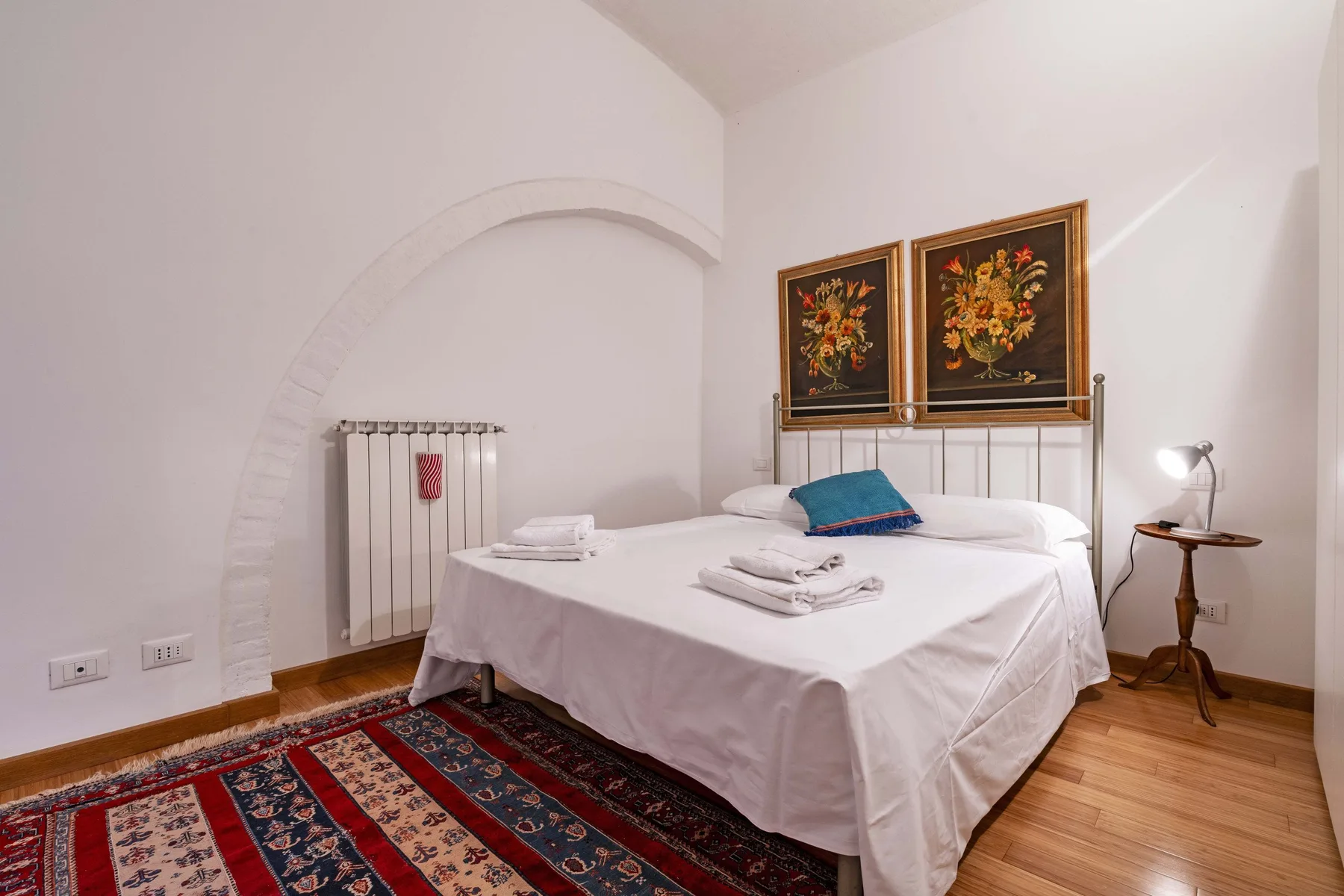 A bedroom with a neatly made bed, framed artwork, and a patterned rug.