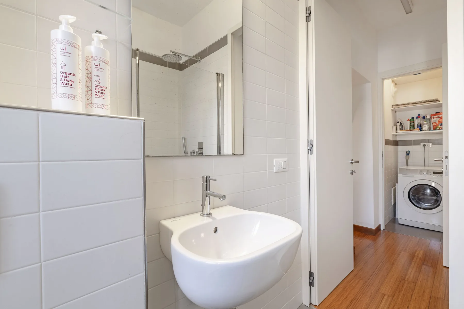 A tiled bathroom with a sink and mirror beside an open doorway.