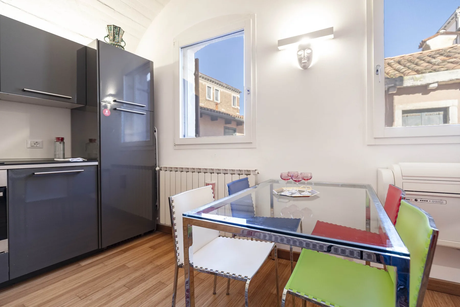 A bright dining area with a glass table and colorful seating beside a compact kitchen.