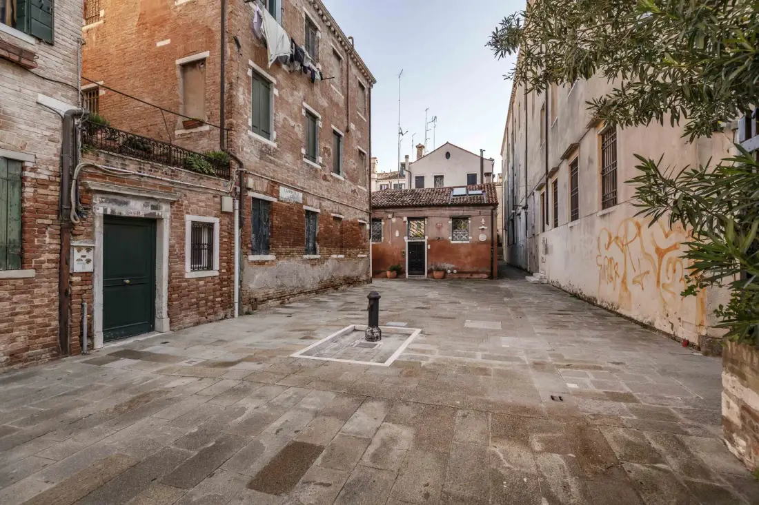 A paved courtyard between brick buildings, with a small fountain in the center.