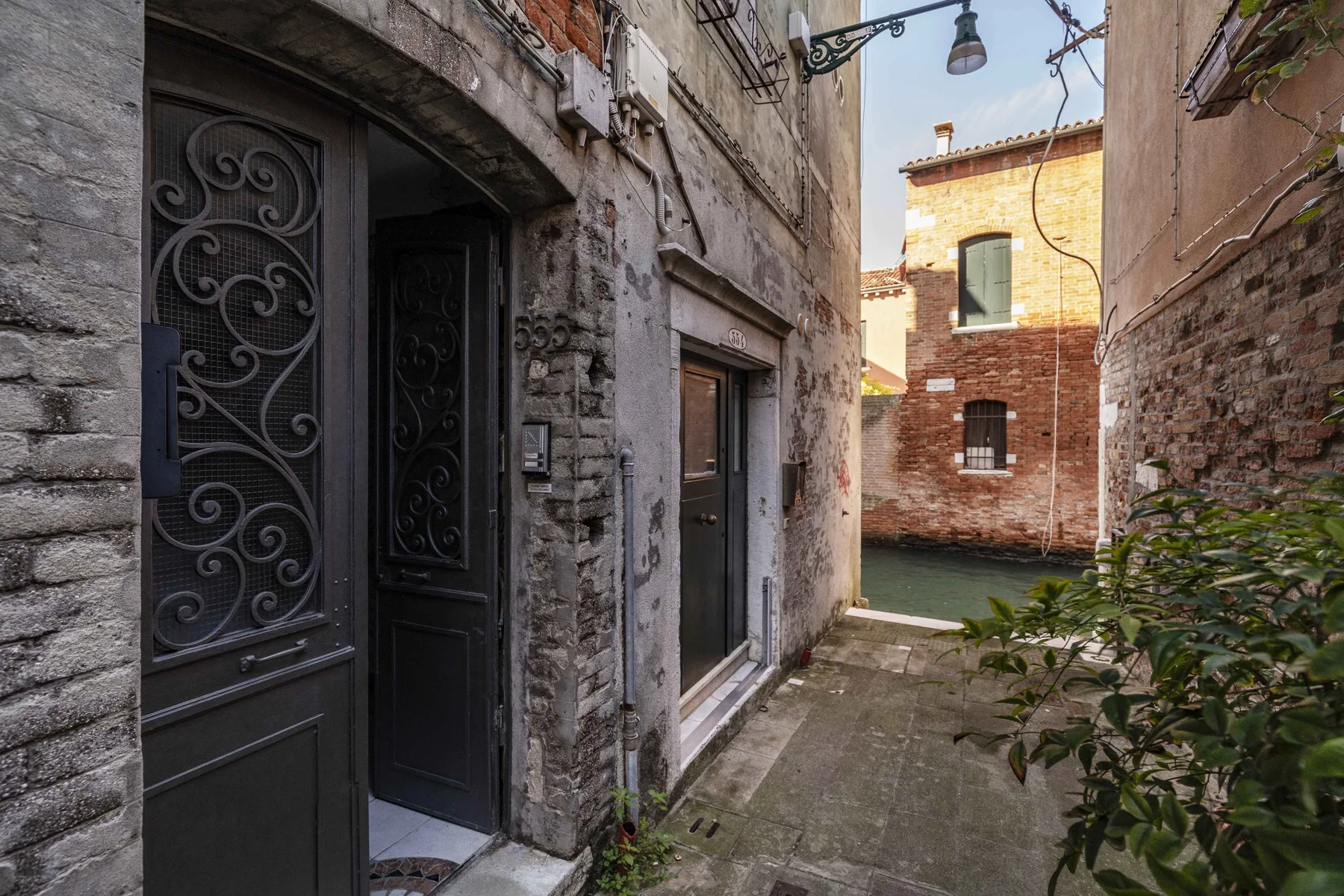 A narrow stone alley passes a dark doorway and opens onto a brick courtyard.