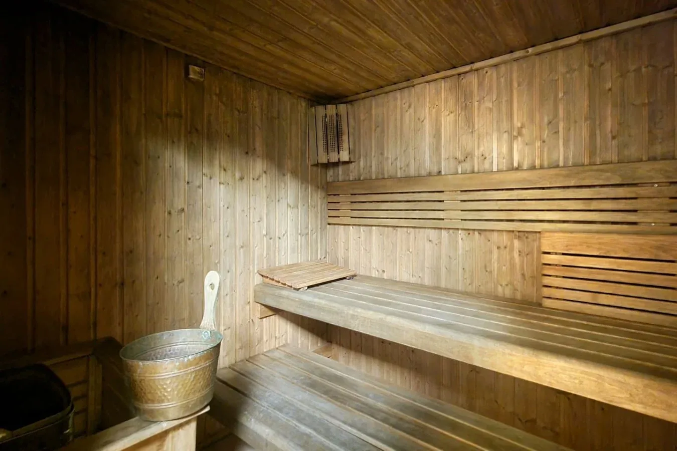 A wood-paneled sauna with tiered wooden benches and a metal bucket.