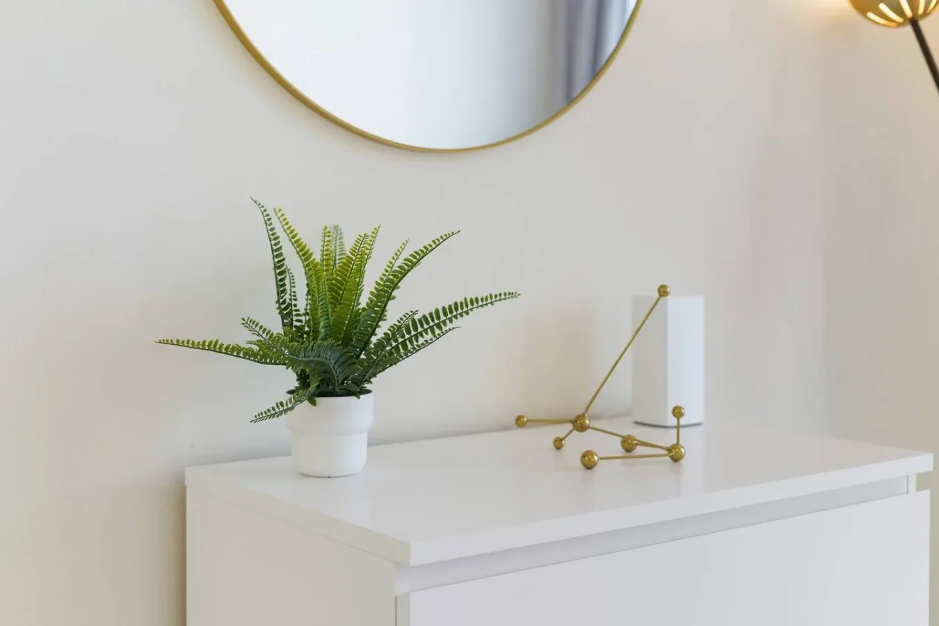 A white dresser holds a potted fern and a small gold decorative sculpture.