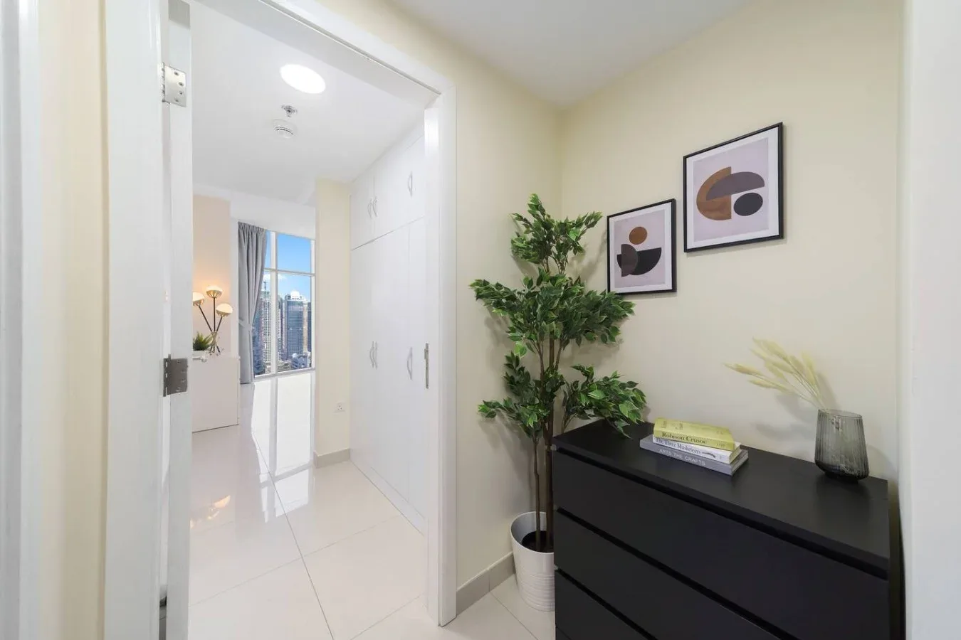 A bright hallway with a black dresser, potted plant, and framed artwork.