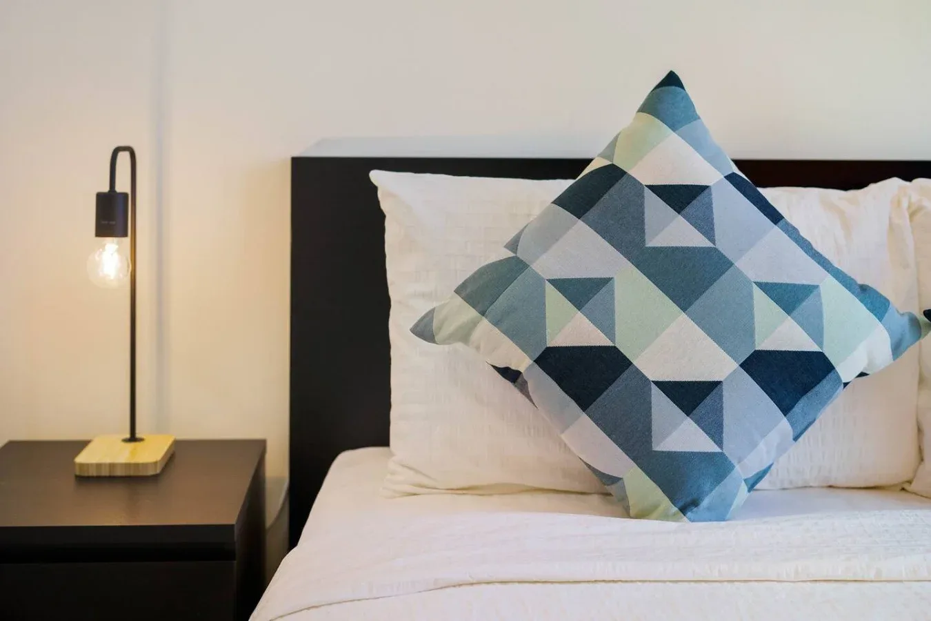 A bedroom scene with white bedding and a blue geometric accent pillow.
