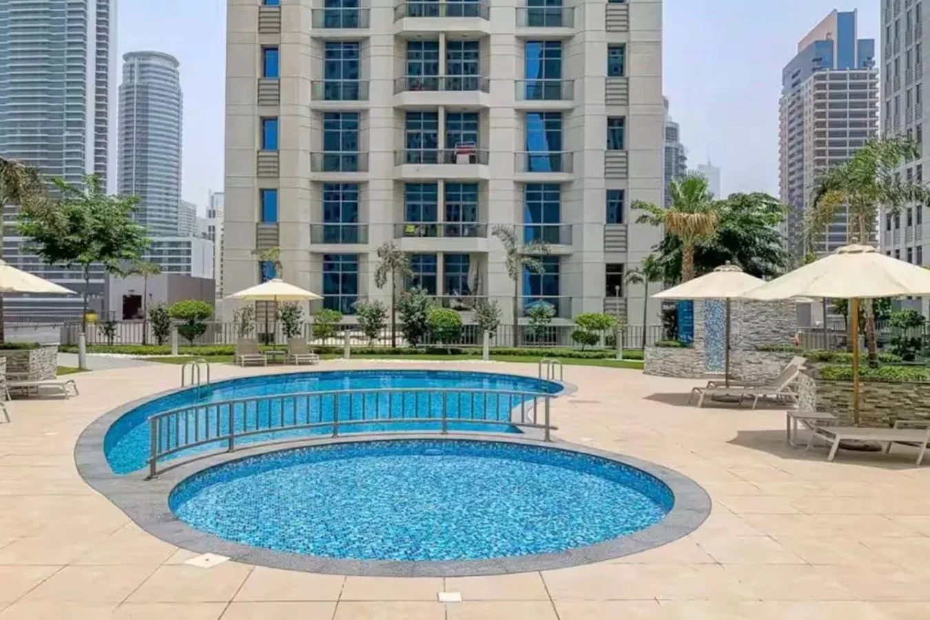 A rooftop swimming pool with a smaller curved pool in front of a high-rise building.