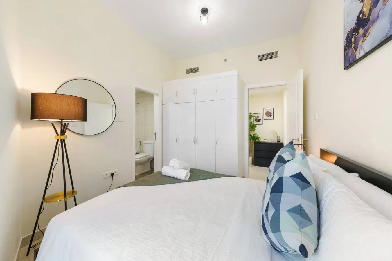A bright bedroom with a neatly made bed and a white built-in wardrobe.
