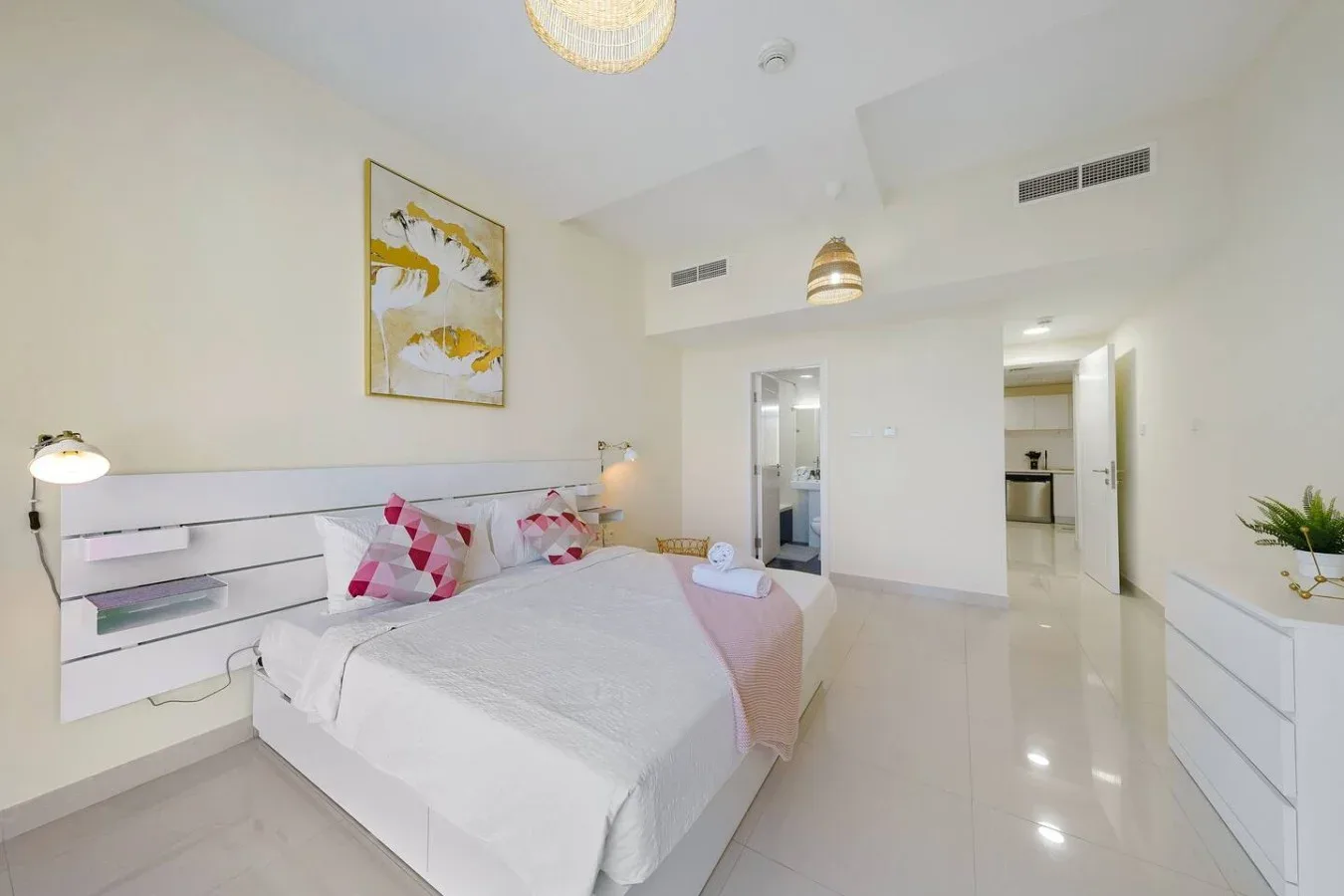 A bright bedroom with a neatly made bed and an open doorway to another room.
