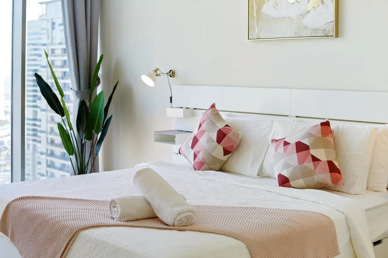 A neatly made bedroom with patterned cushions and a large window.