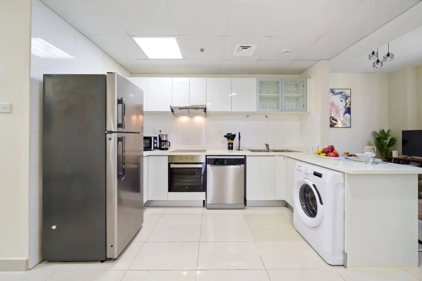 A bright kitchen with white cabinets, stainless steel appliances, and a washing machine.