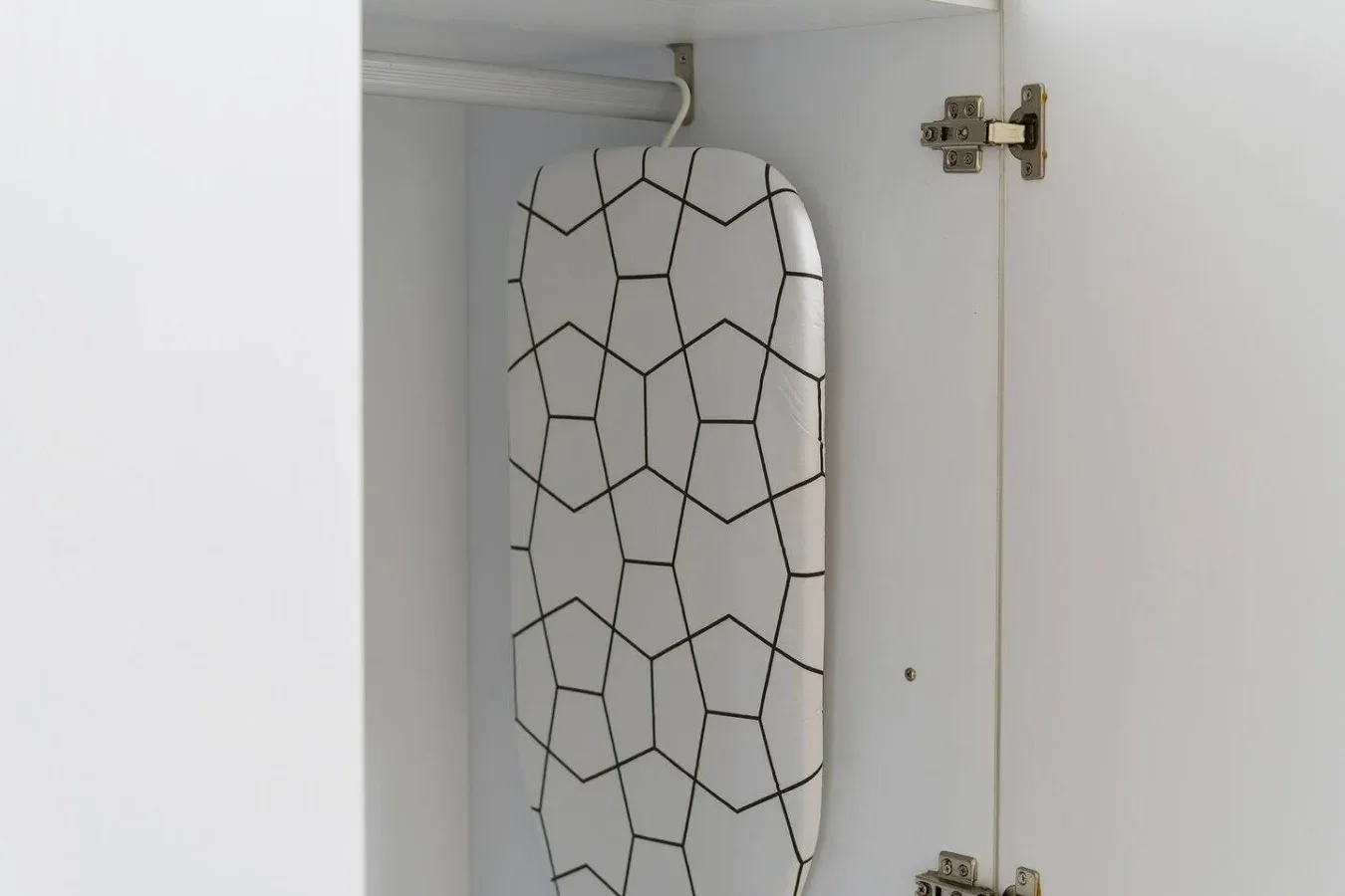 An ironing board with a geometric pattern is stored inside a white cabinet.