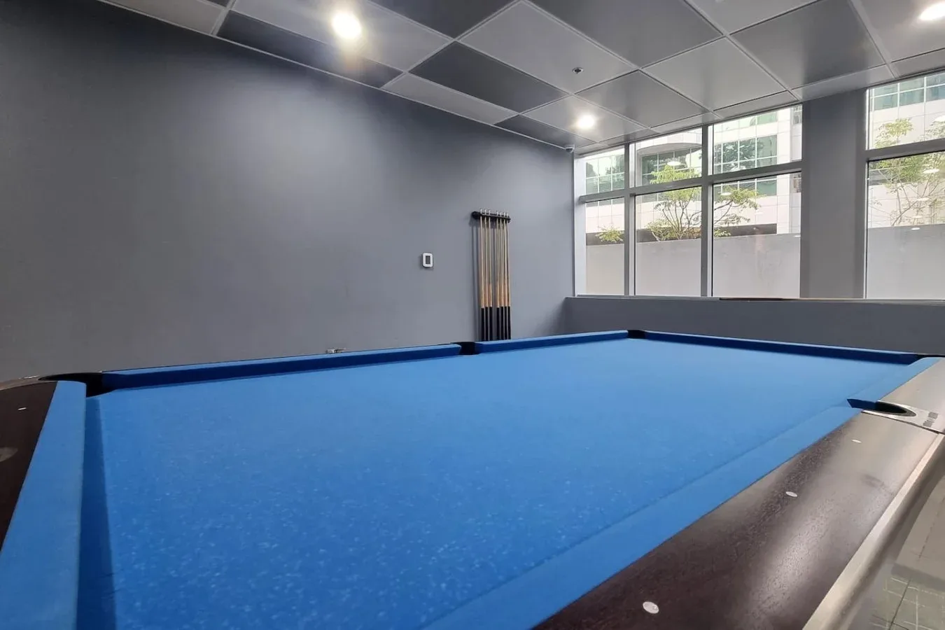 A blue-felt pool table fills a room with large windows.