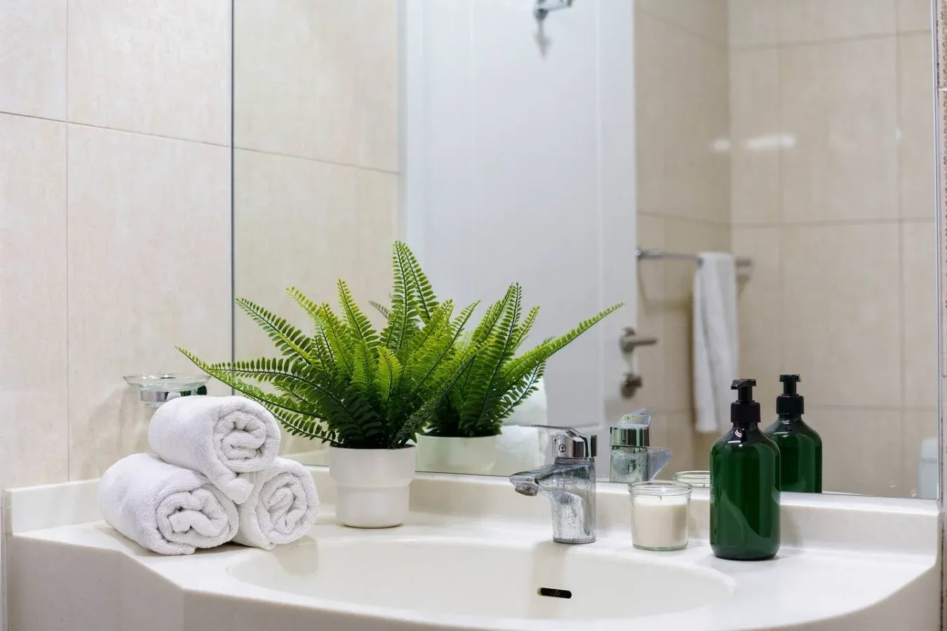 A bathroom vanity with folded towels, a potted fern, and toiletries.