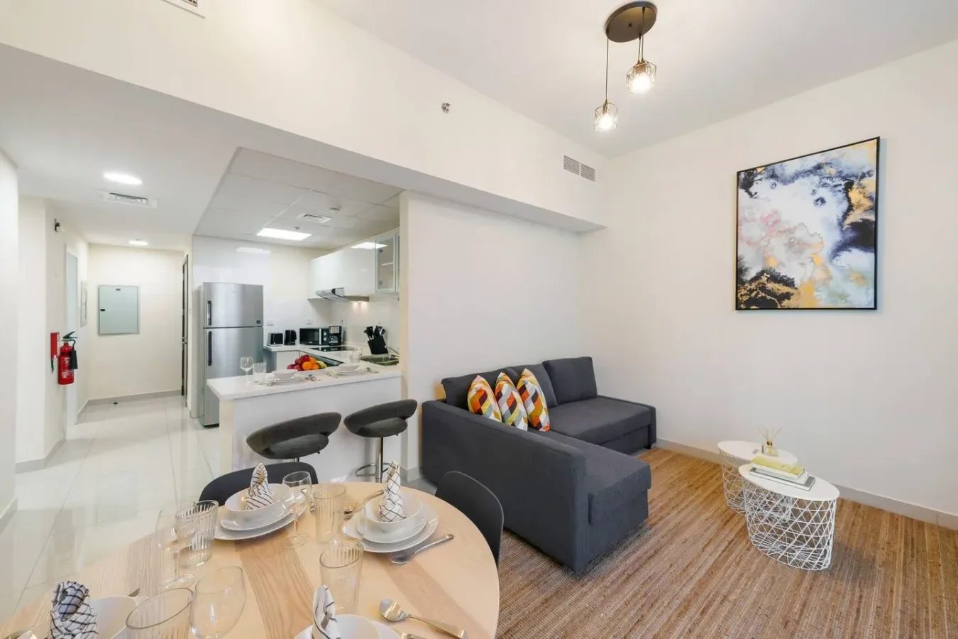 An open-plan living and dining area with a gray sectional beside a compact kitchen.