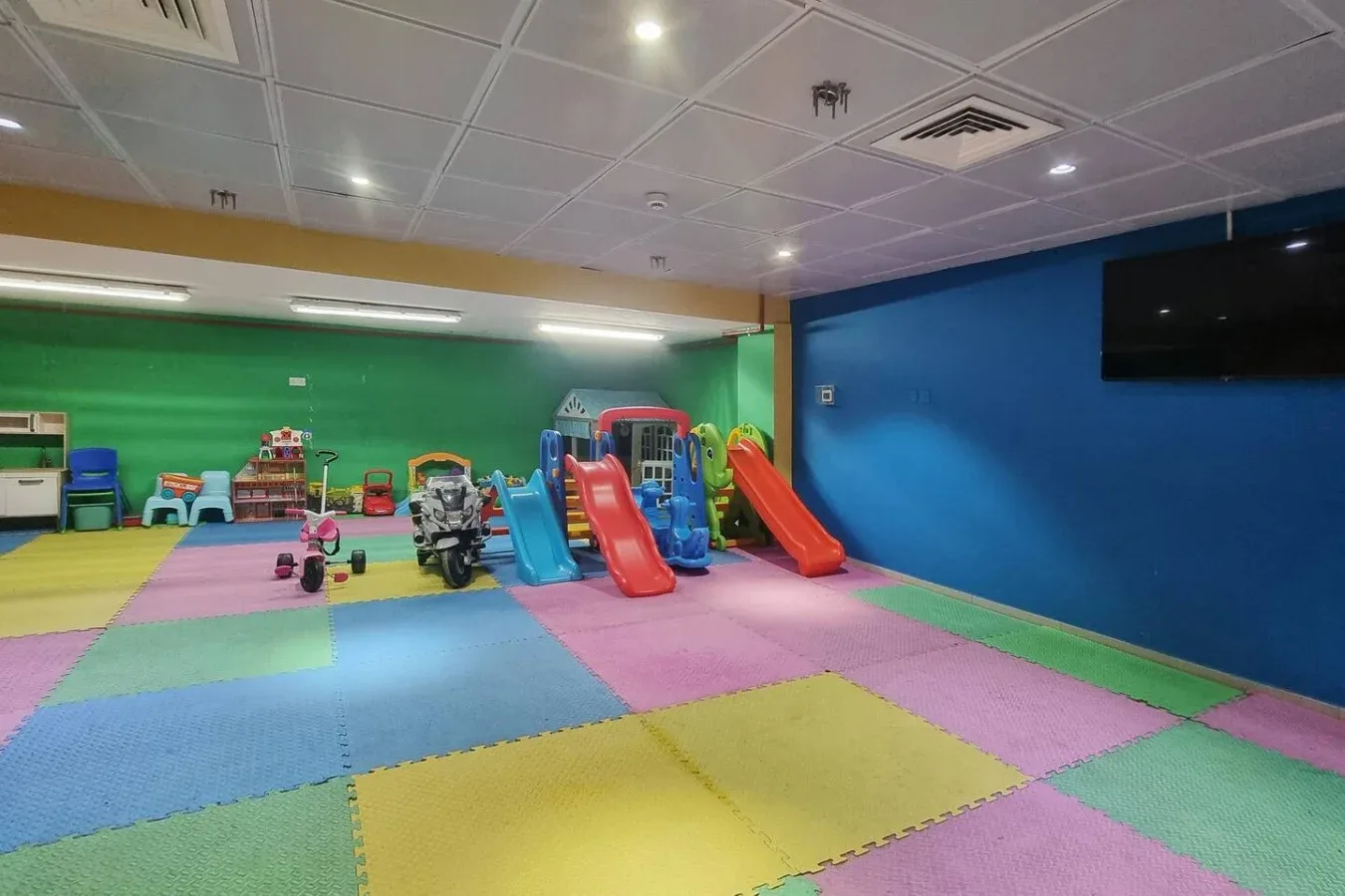 A colorful indoor playroom with slides and padded floor mats.
