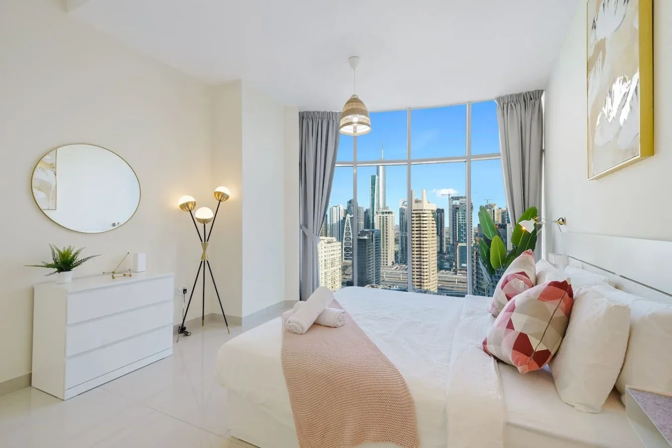 A bright bedroom with a bed facing large windows overlooking the city skyline.