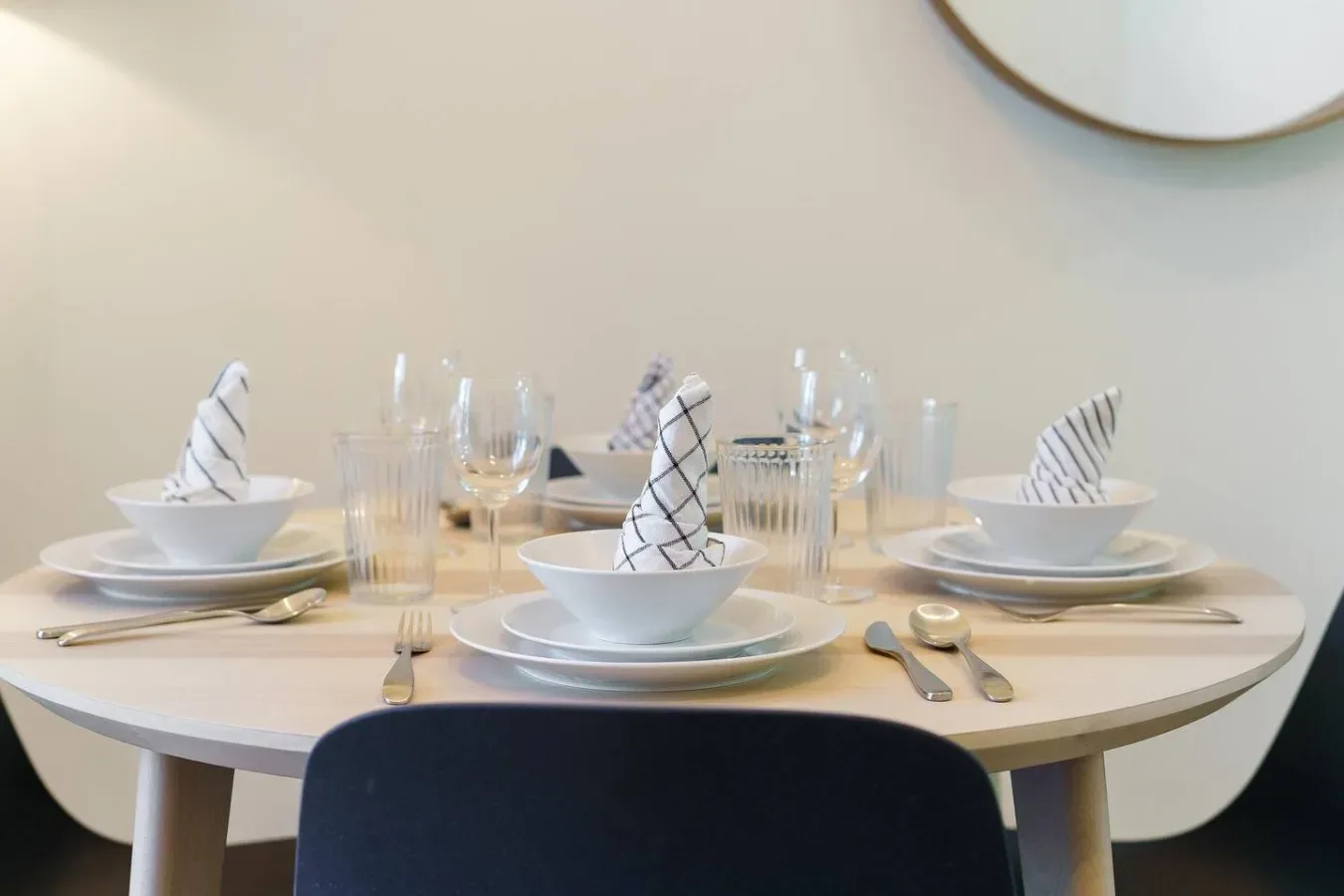 A dining table is set with plates, glassware, and folded napkins.