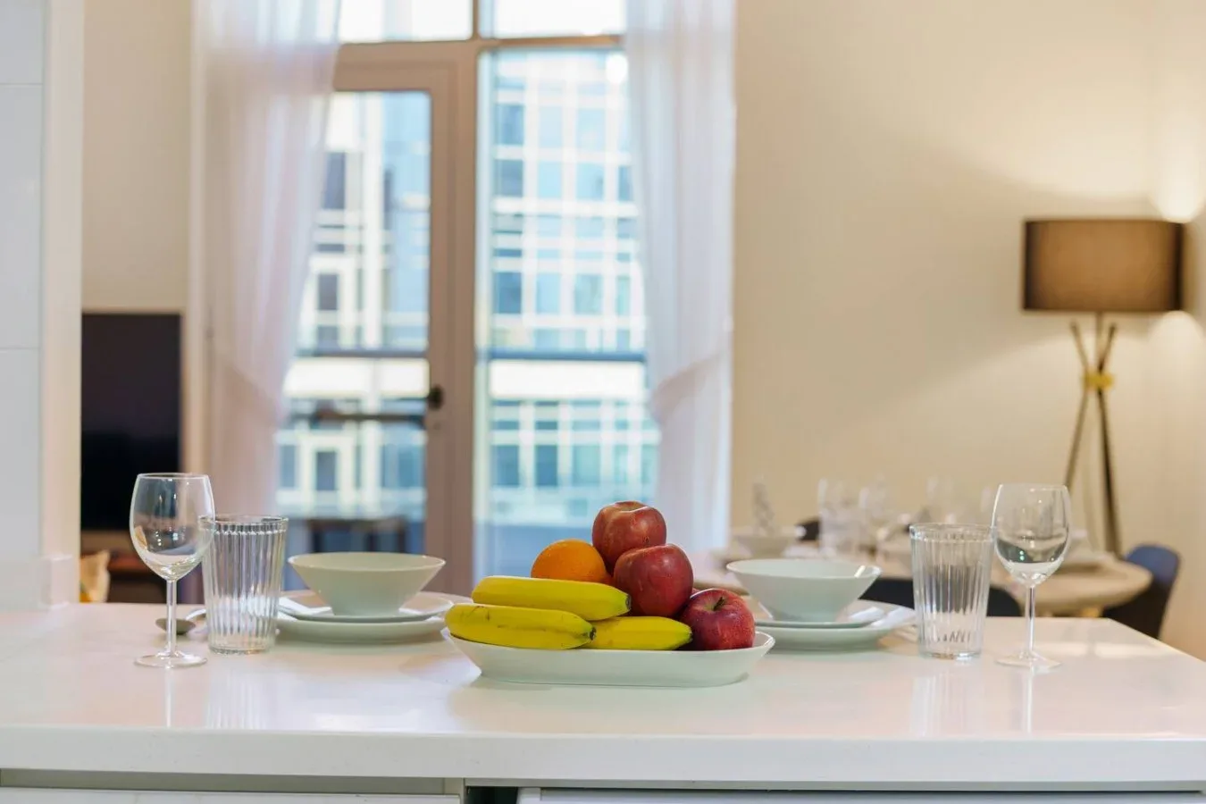A dining table is set with dishes and fruit in front of a large window.