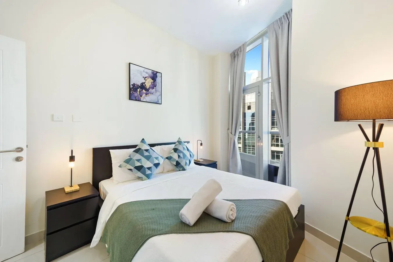 Bedroom with a neatly made bed and tall windows.
