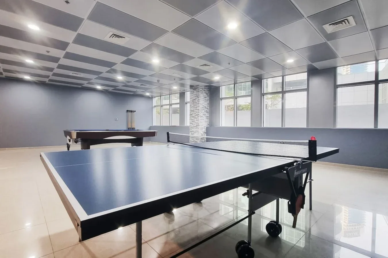 A spacious recreation room with table tennis tables and large windows.