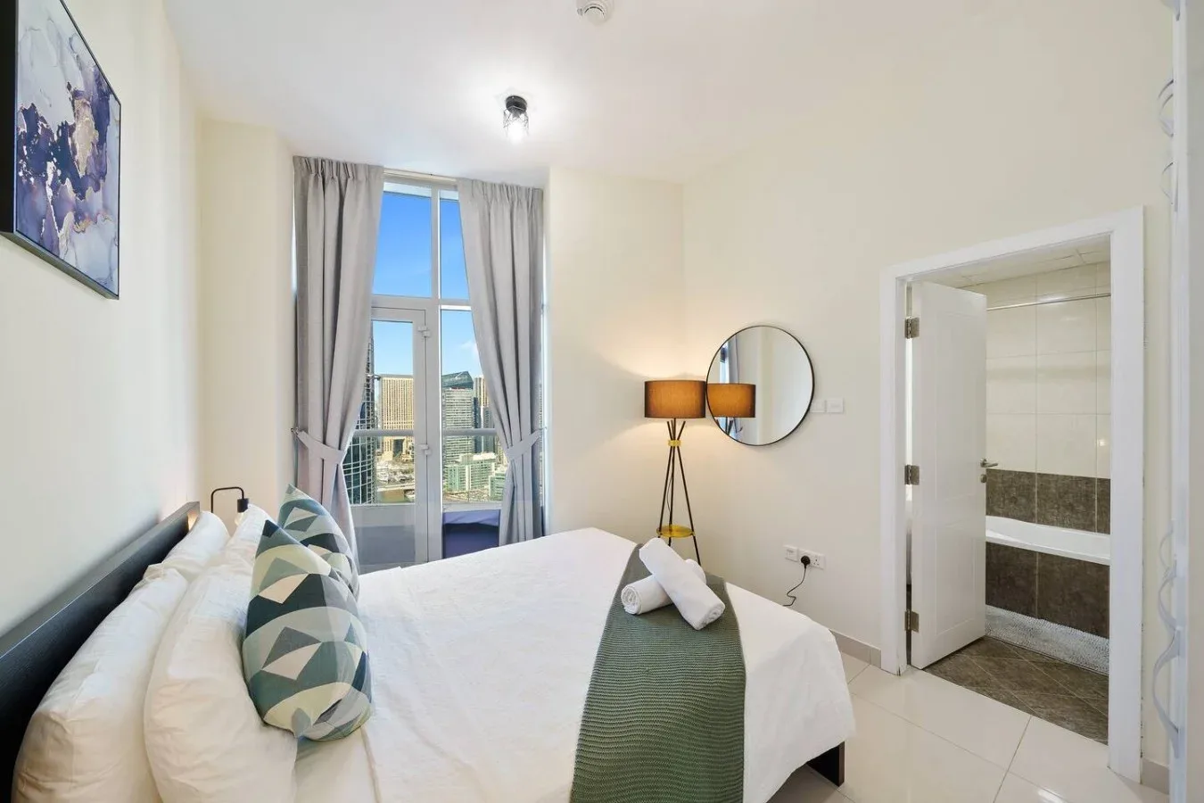 A bright bedroom with a neatly made bed and an open doorway to the bathroom.