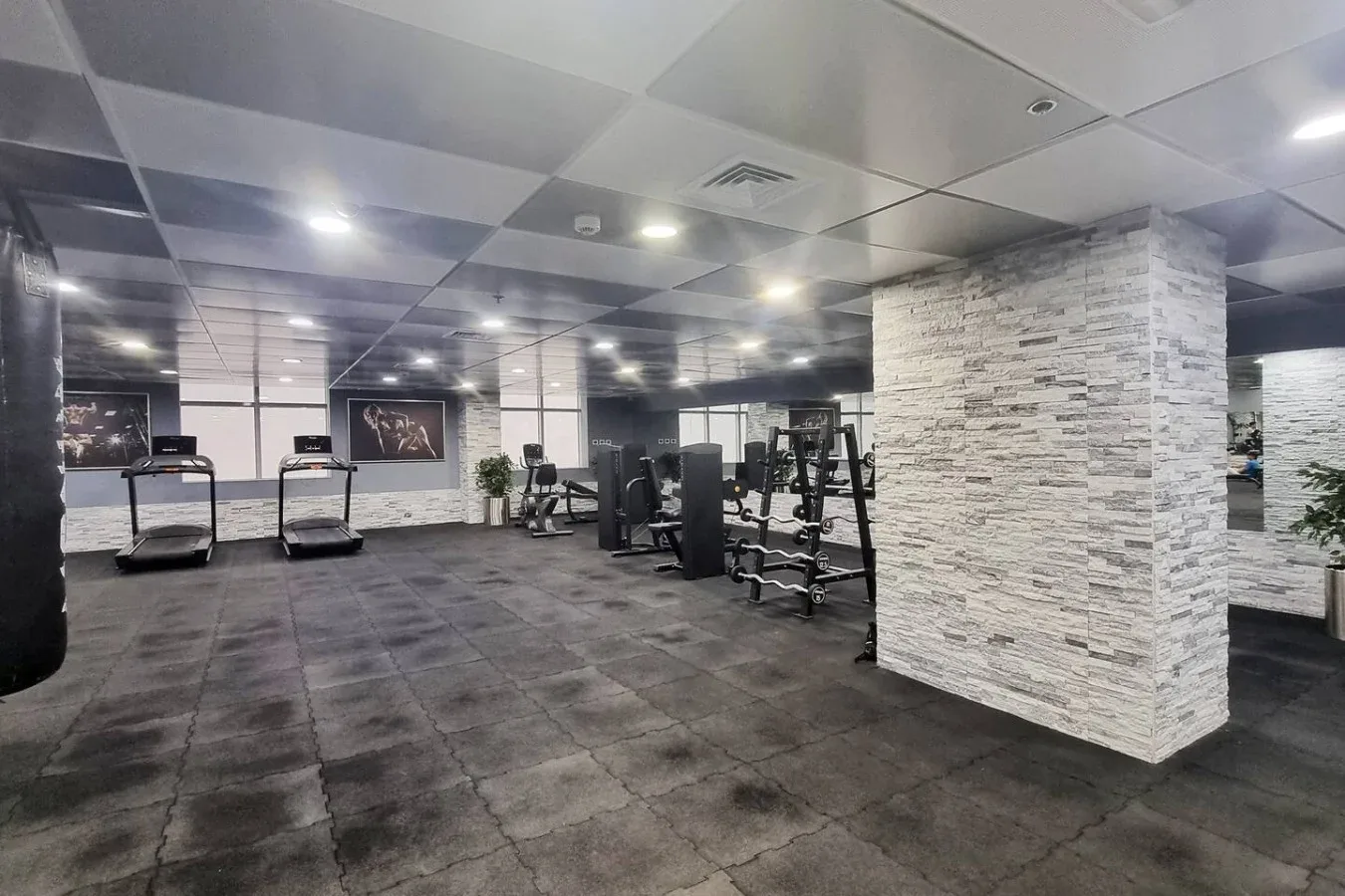 A spacious gym with exercise machines and treadmills under a tiled ceiling.