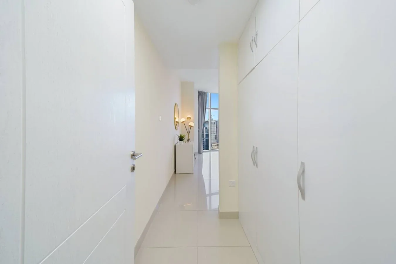 A bright hallway with white built-in cabinets and a view toward a window.