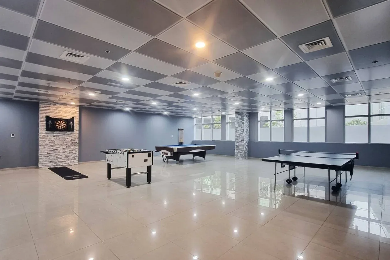 A spacious recreation room with several table tennis tables and large windows.