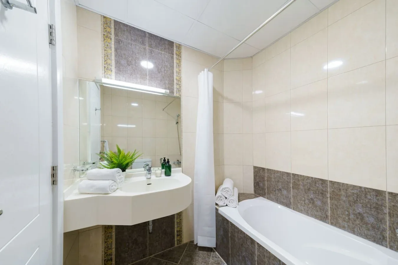 A tiled bathroom with a bathtub, sink, and mirror.