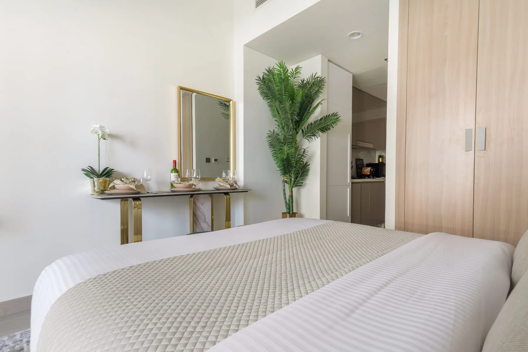 Dormitorio con una cama bien tendida, una planta alta y un tocador.