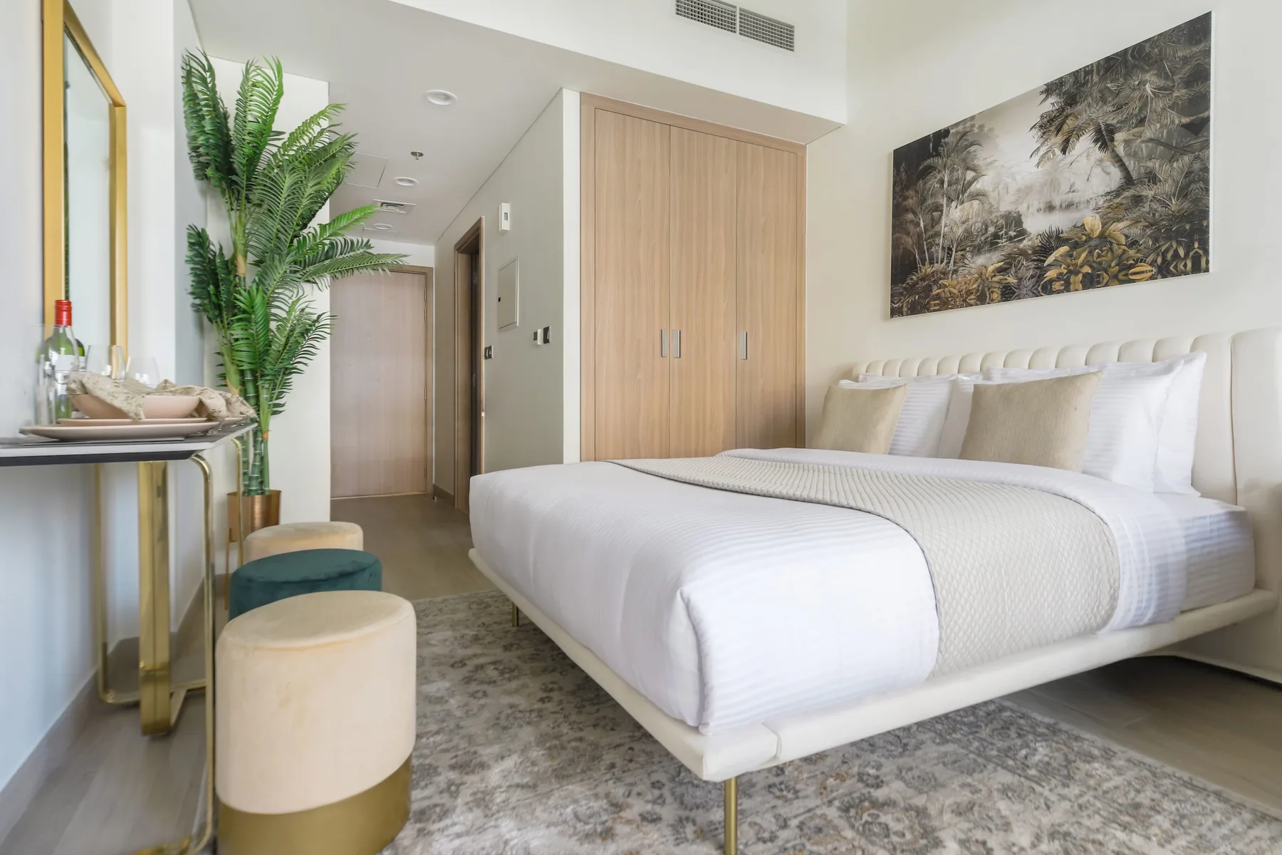 A bright bedroom with a neatly made bed, wood wardrobe, and potted greenery.