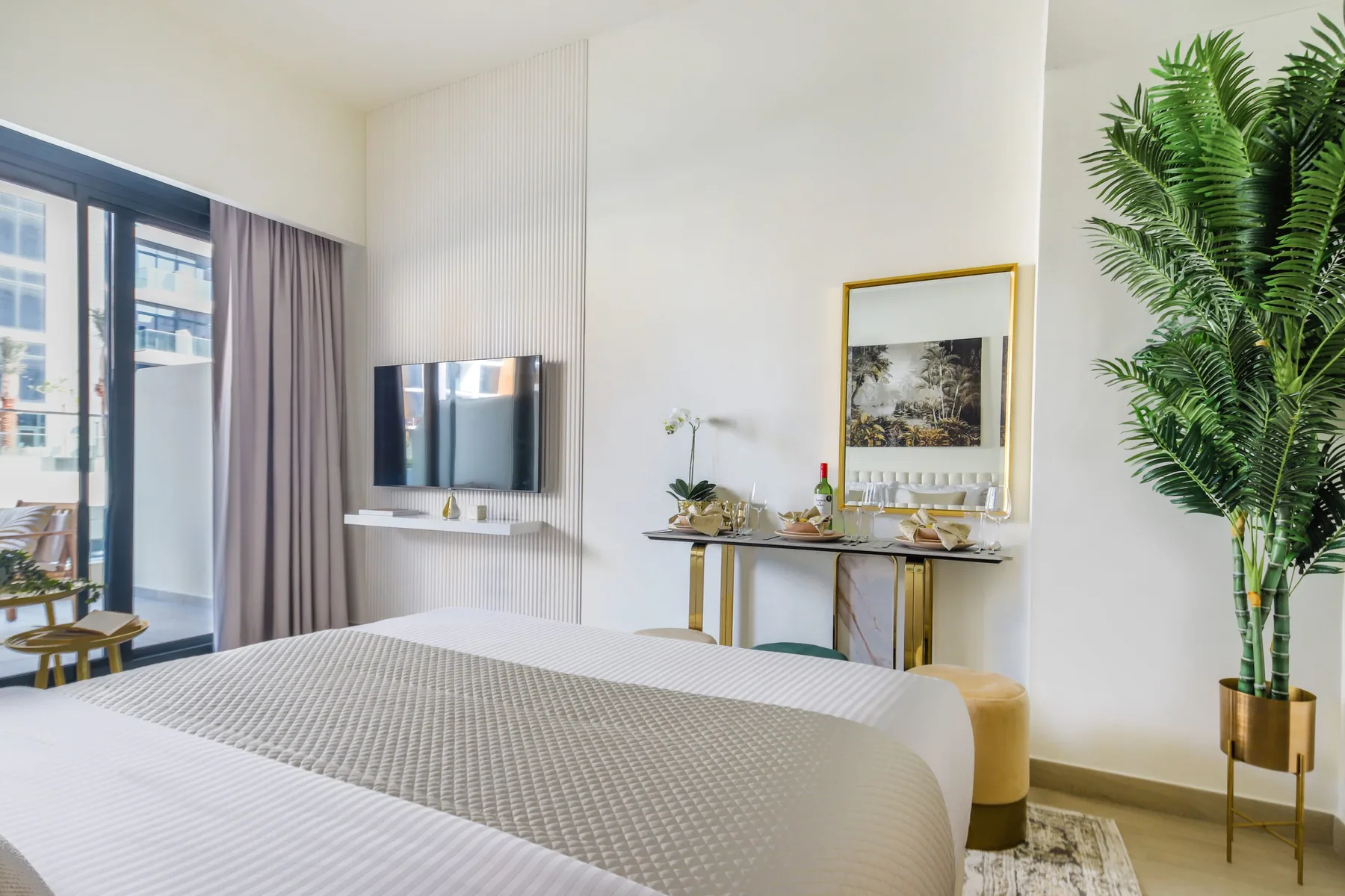 Un dormitorio luminoso con una cama, un televisor montado en la pared y una consola pequeña.