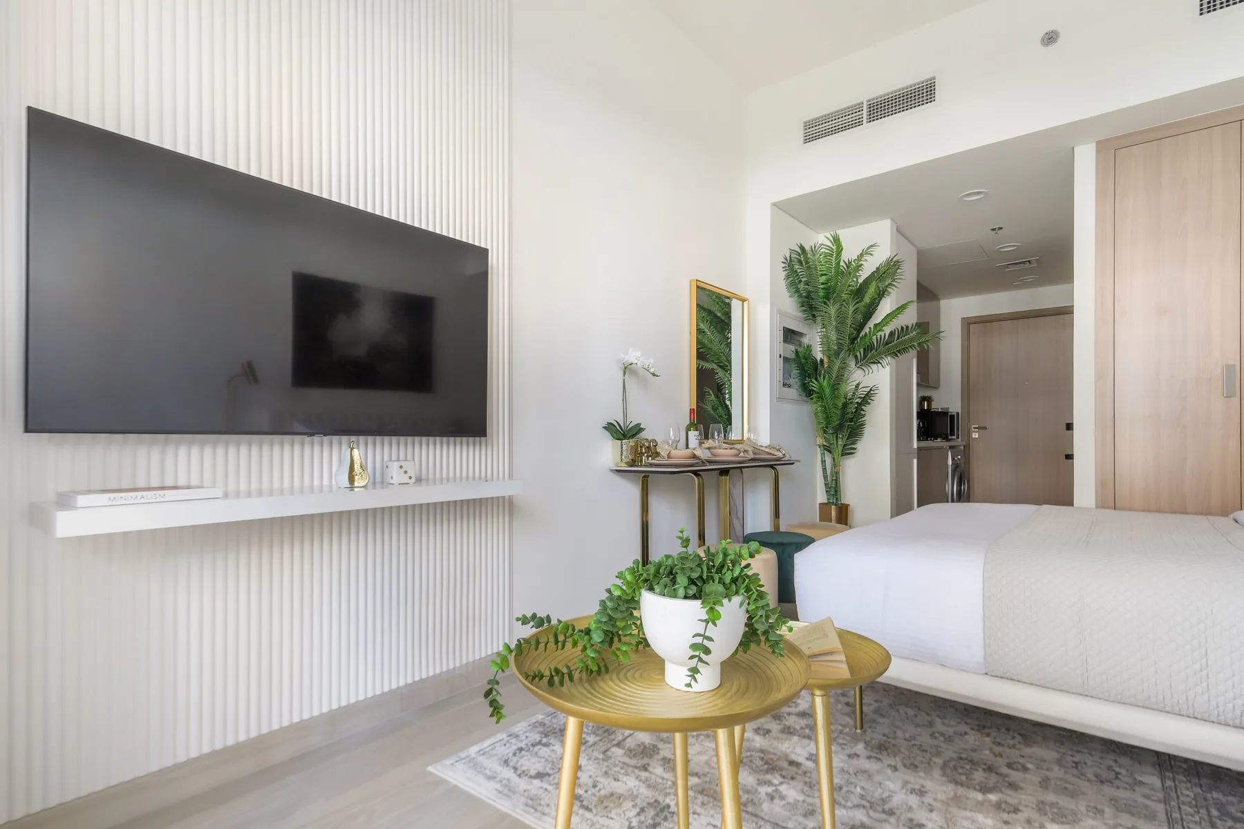 Un dormitorio luminoso con un televisor grande en la pared y asientos junto a la cama.