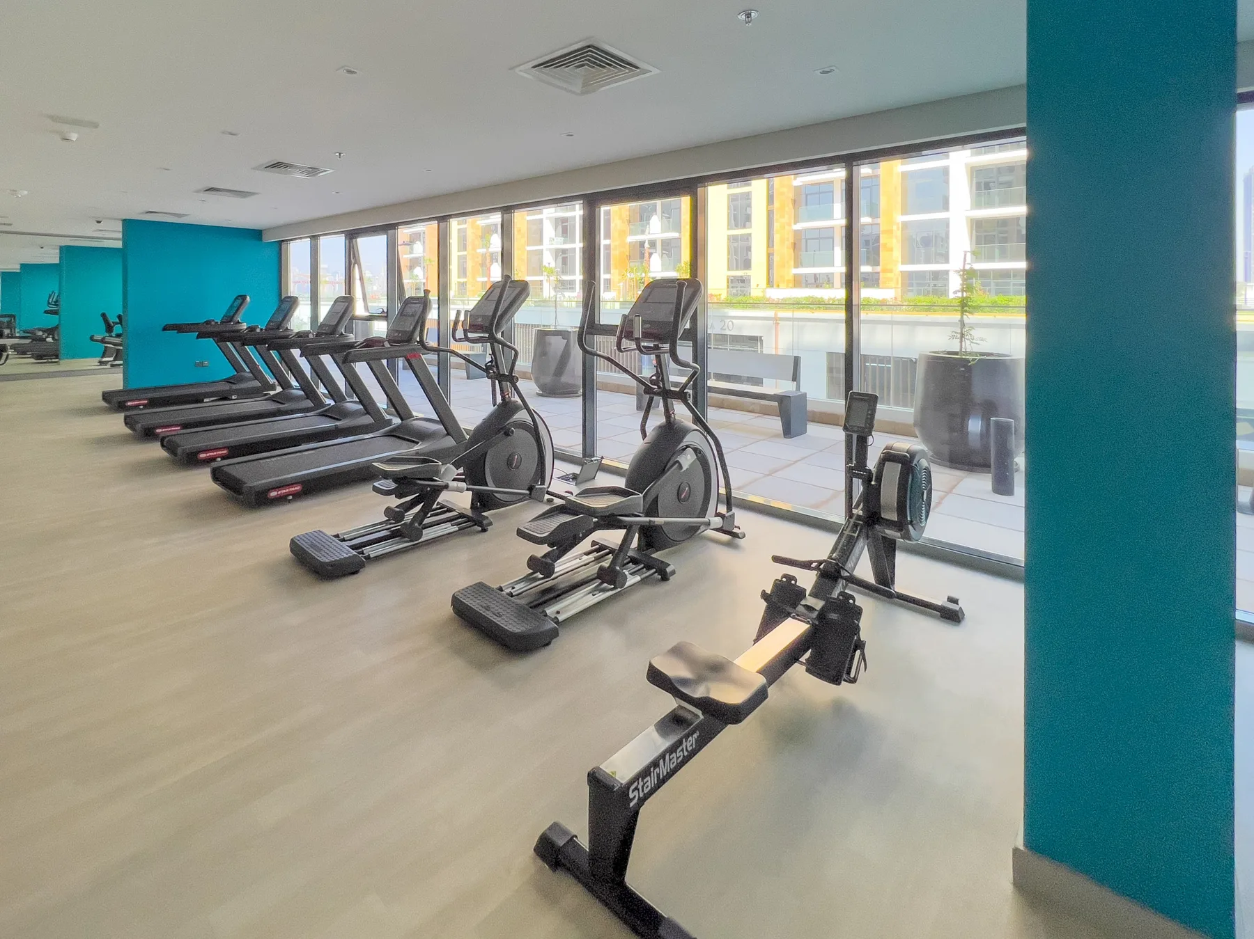 Un gimnasio con cintas de correr y máquinas de ejercicio junto a grandes ventanas.