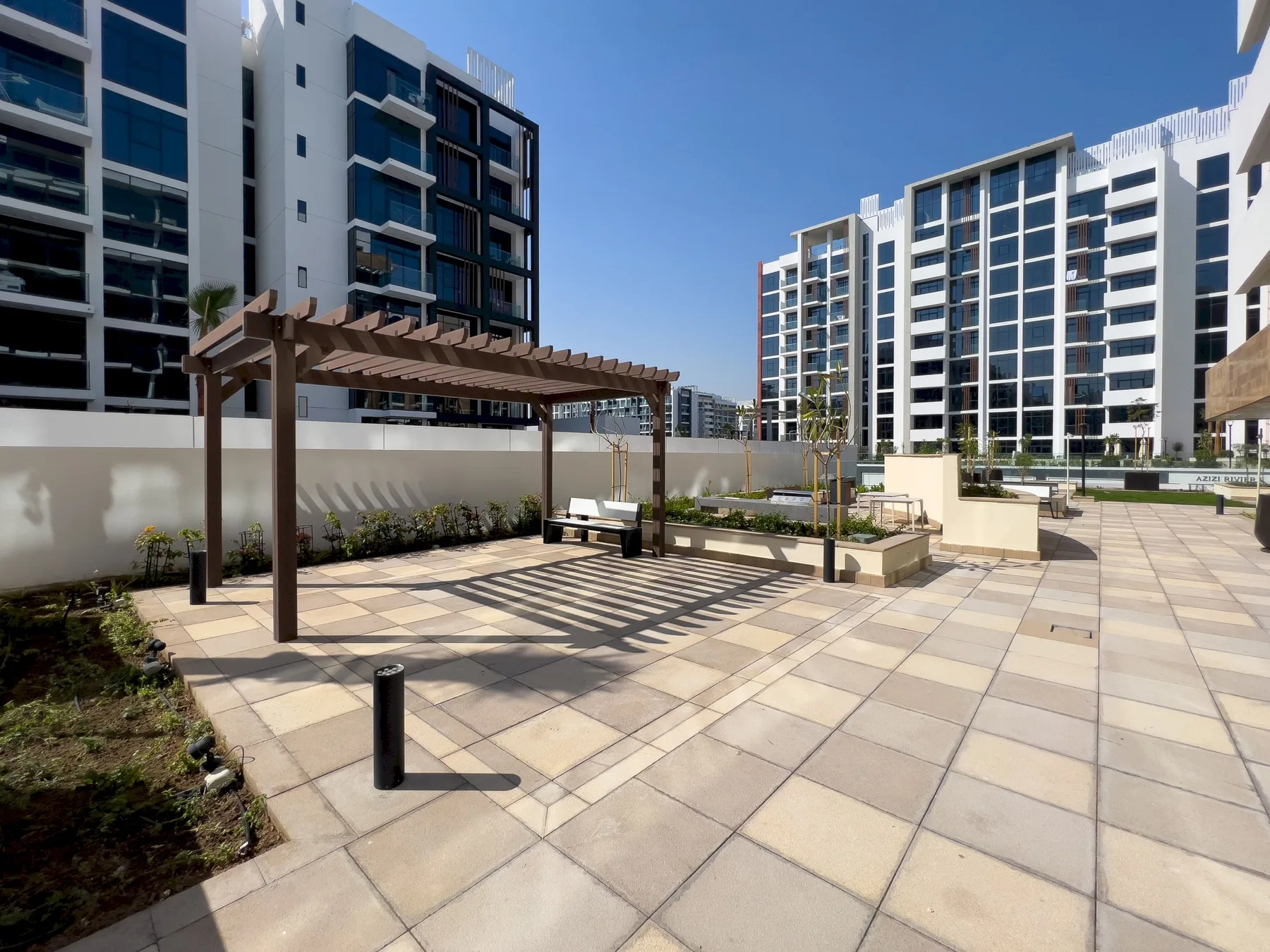 Un patio exterior pavimentado cuenta con una pérgola de madera y edificios de apartamentos alrededor.