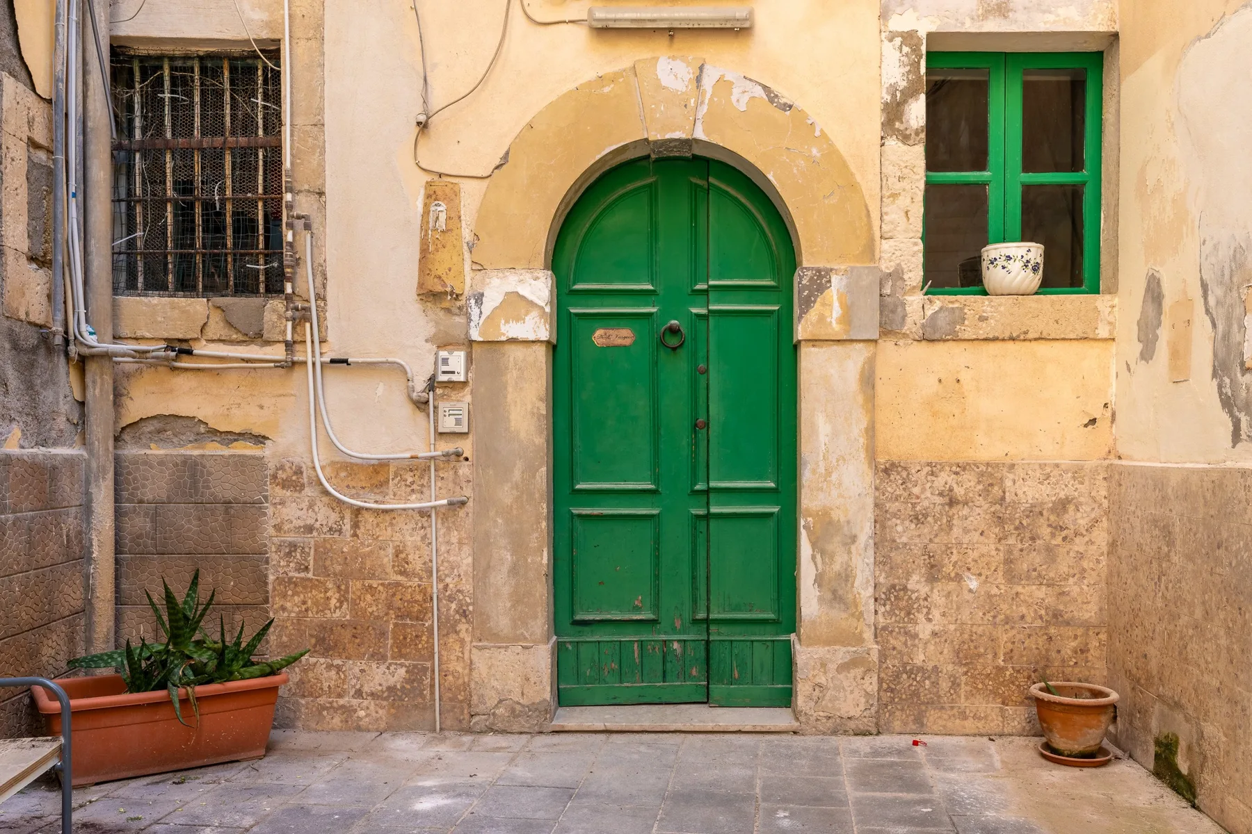 A green arched door set in a weathered yellow courtyard wall.