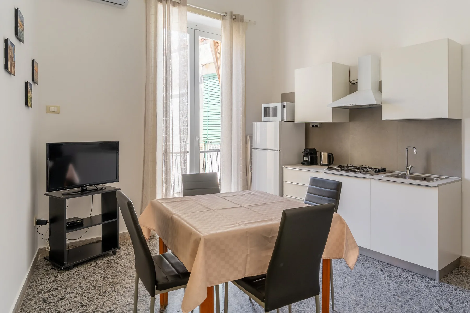 A dining table and seating sit in a bright room with a compact kitchen.