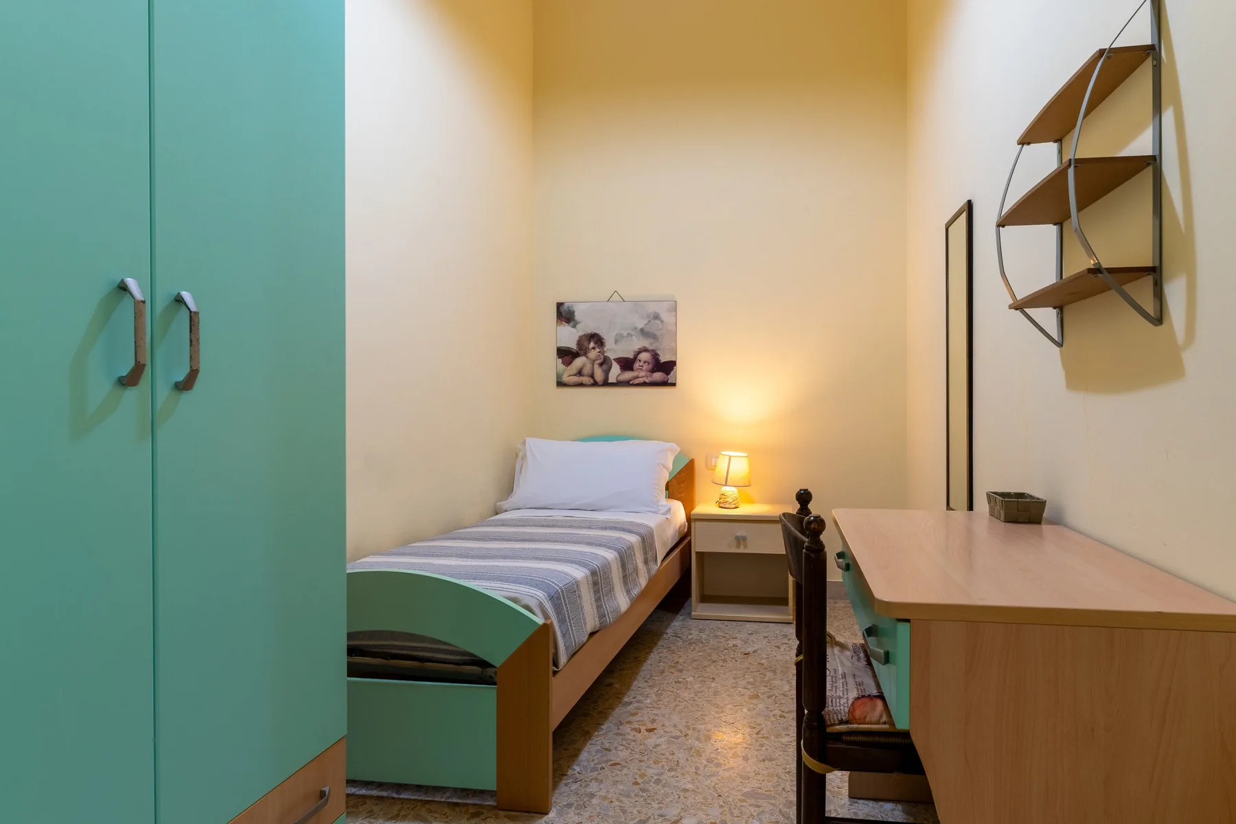 Un dormitorio compacto con una cama individual, un escritorio y un estante de pared.