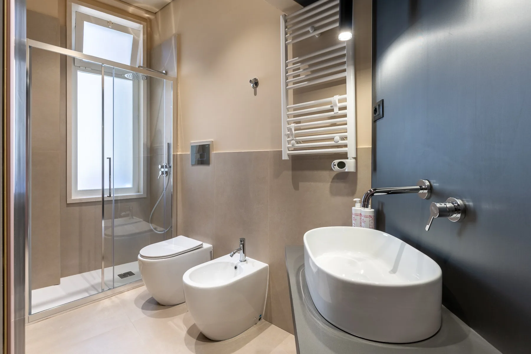 A modern bathroom with a glass shower, toilet, bidet, and bathtub.