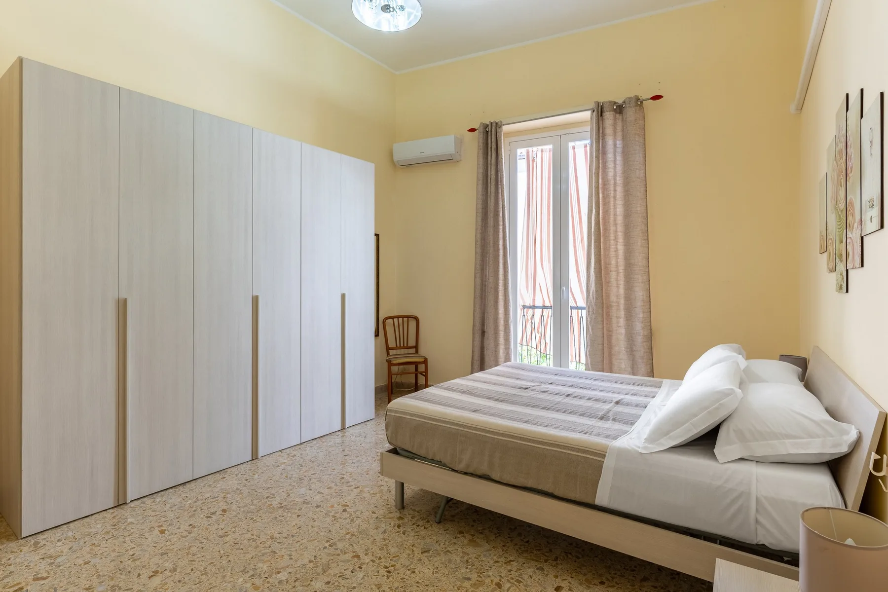 Un dormitorio con una cama junto a un armario grande y ventanas altas con cortinas.