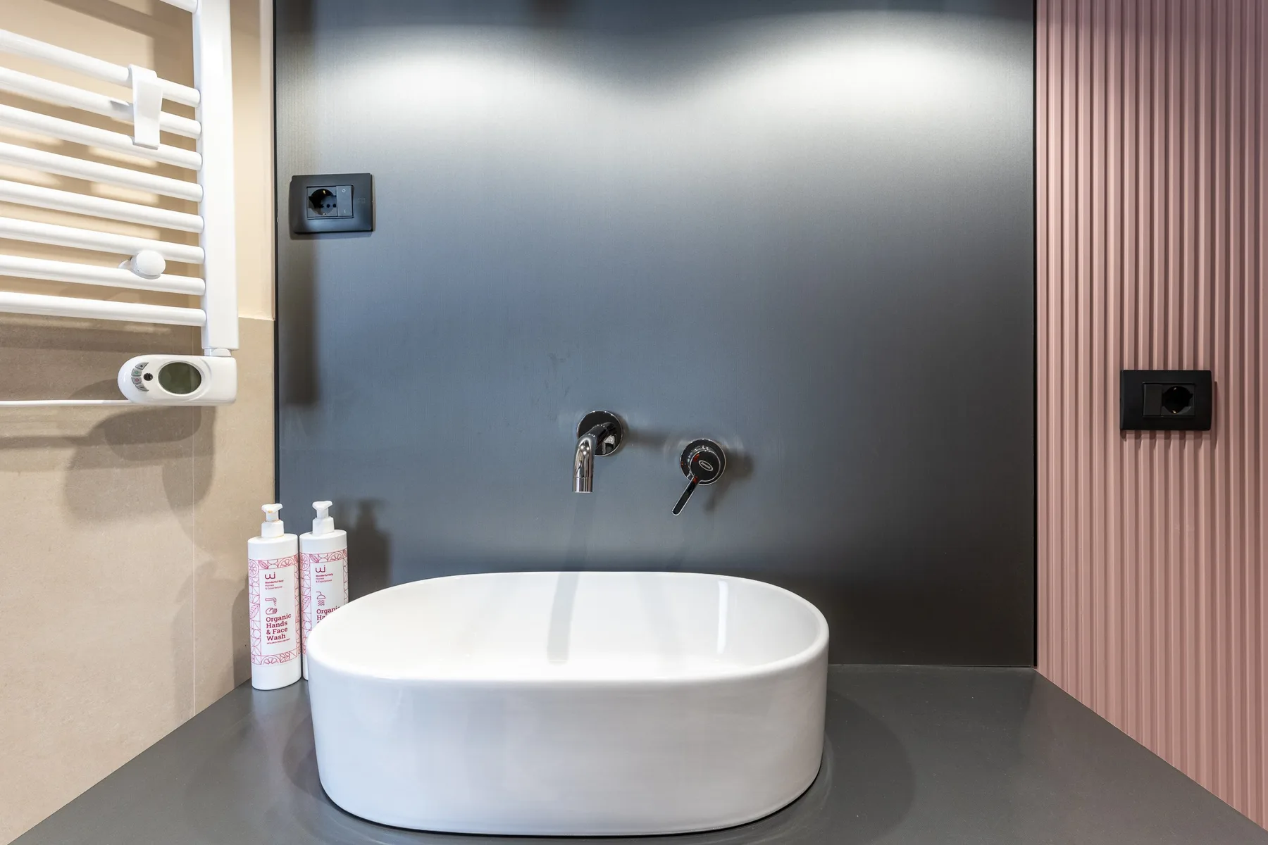 A modern bathroom vanity with a white vessel sink against a dark wall.