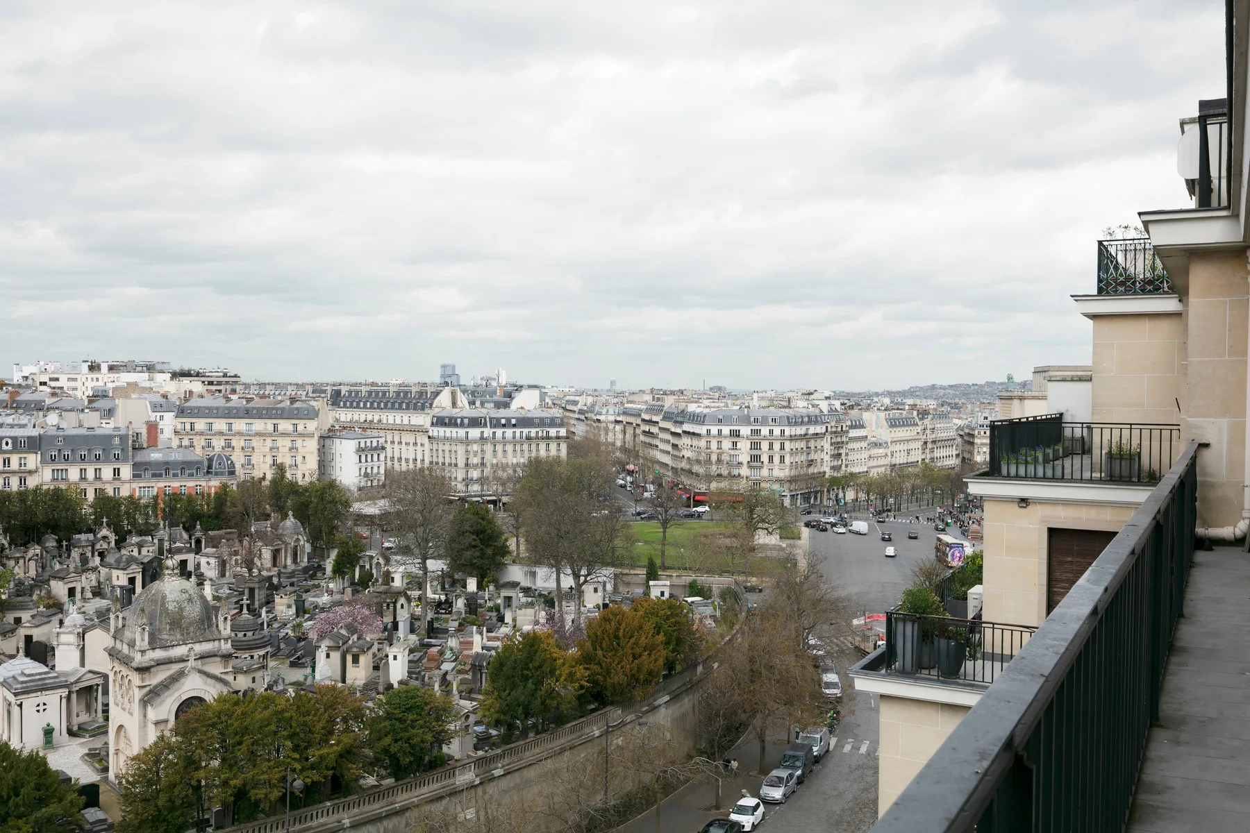 Urban balcony overlooking a tree-lined cemetery and surrounding city buildings.