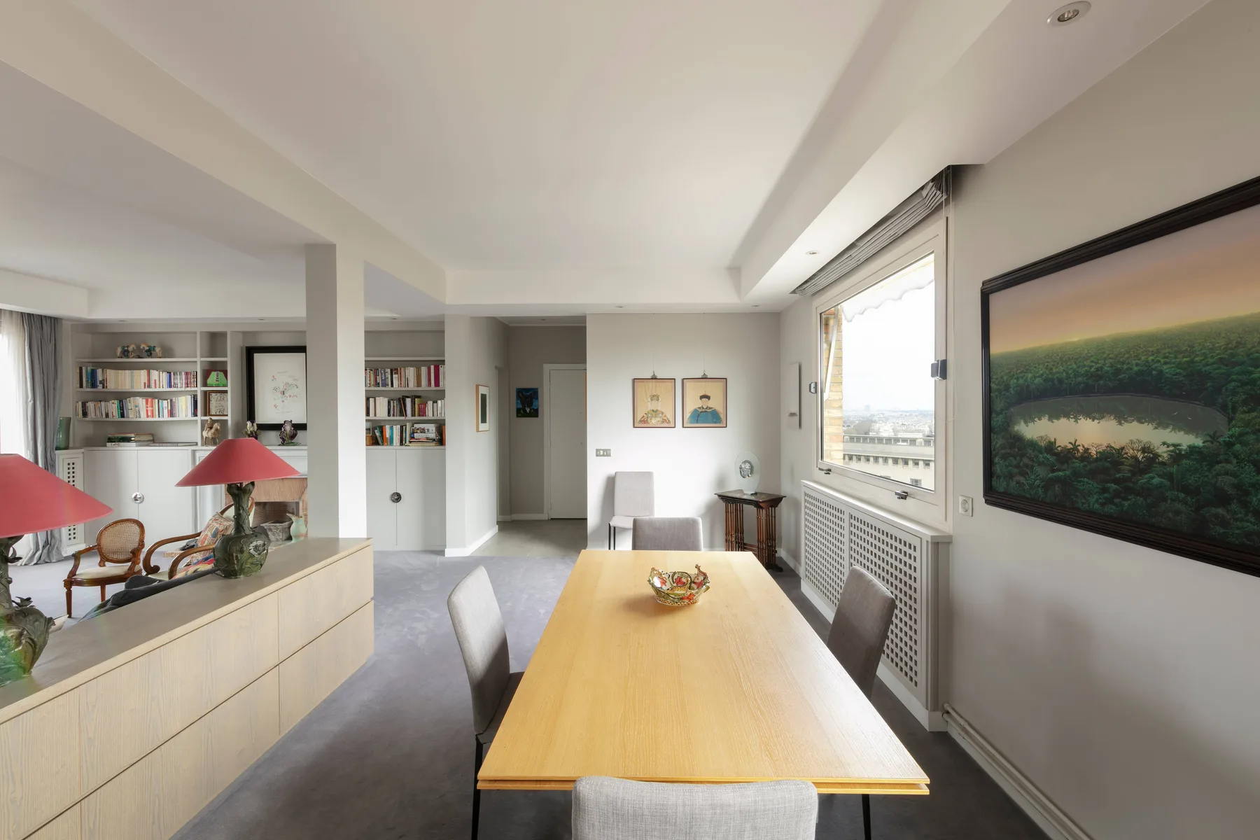 A bright dining area with a long table, built-in shelves, and large windows.