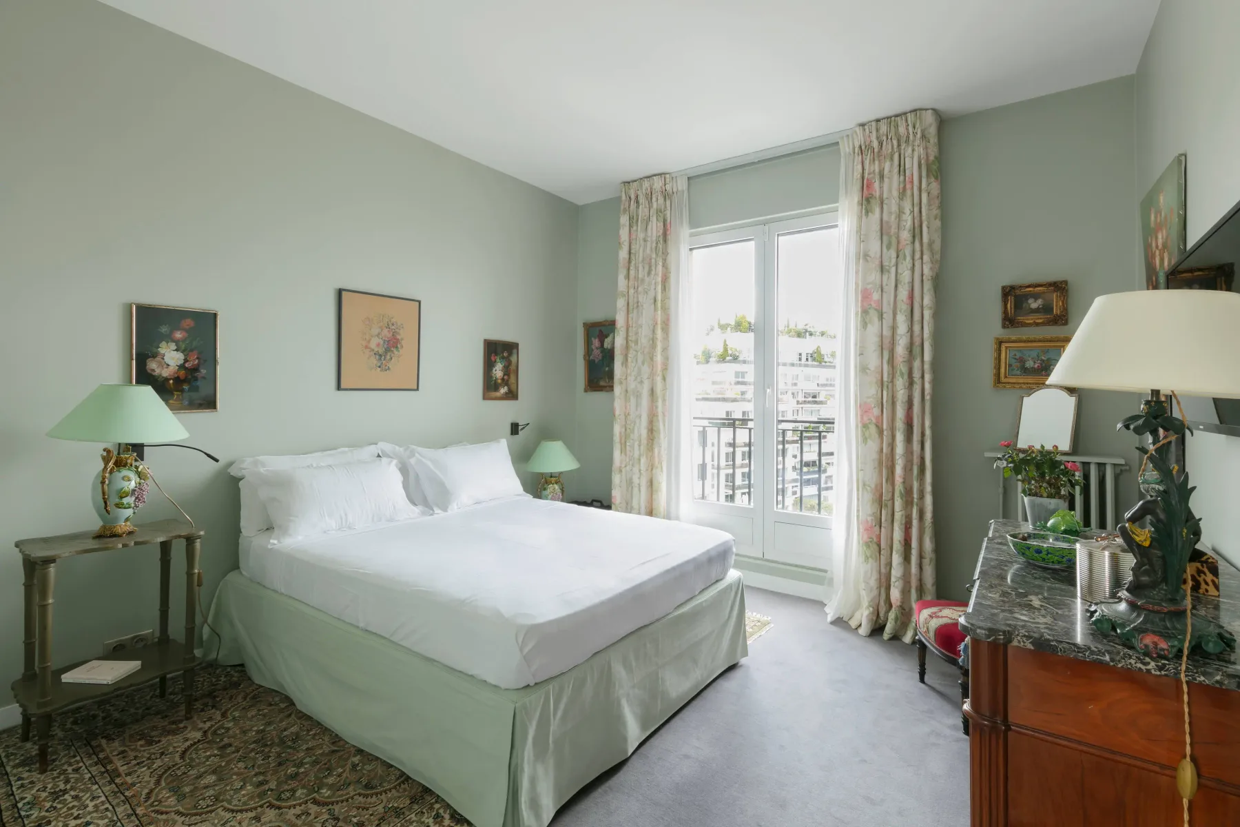 A bedroom with a neatly made bed and tall windows opening onto a balcony.