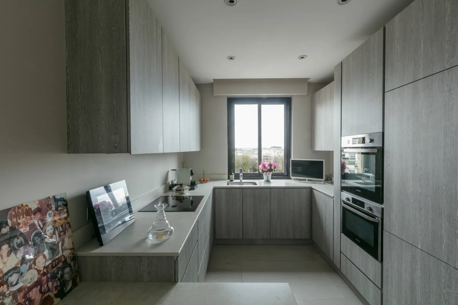 A modern kitchen with gray cabinetry, a countertop, and a window at the far end.